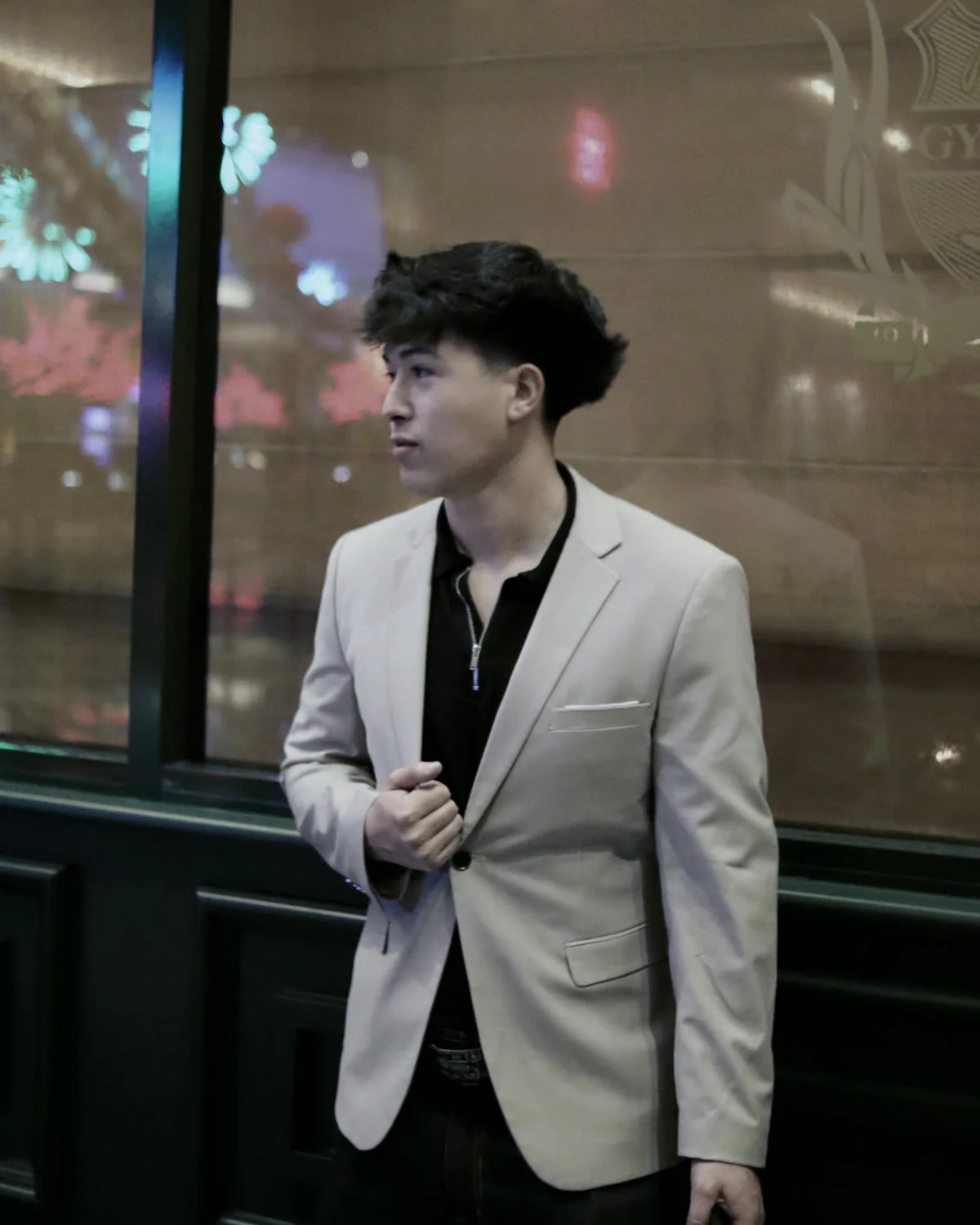 Jordan Lopez in a light blazer, looking out past a window at night