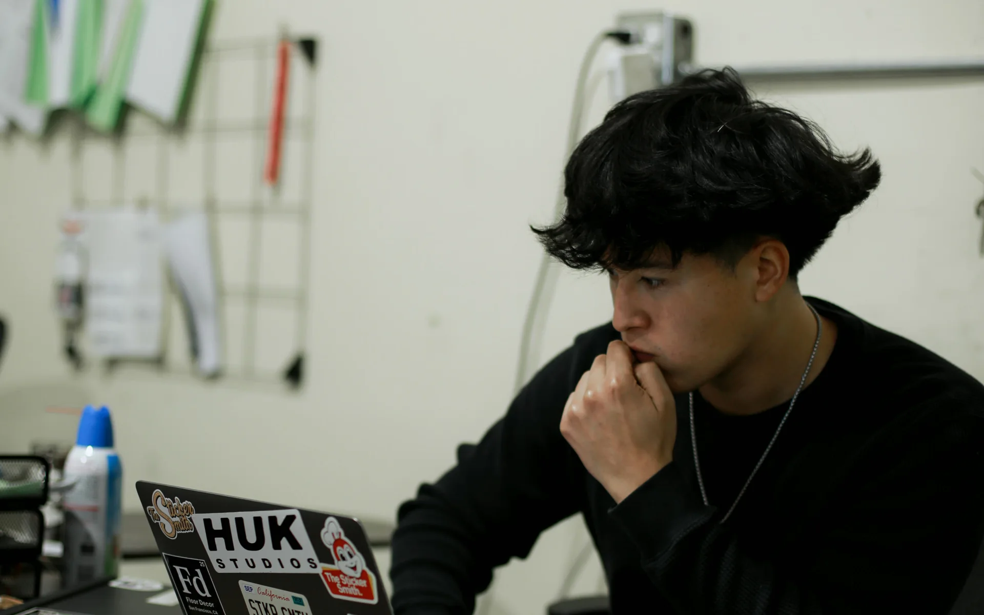Jordan Lopez at his desk, hand at his chin, working on a laptop covered in client stickers