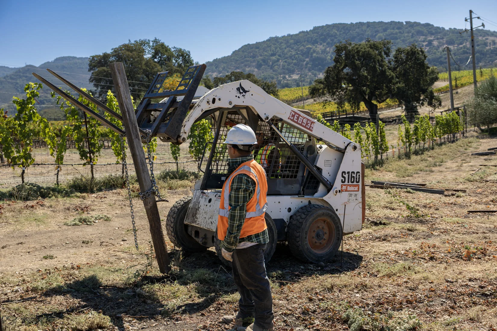 Daytime crew and a skid steer under hills and blue sky